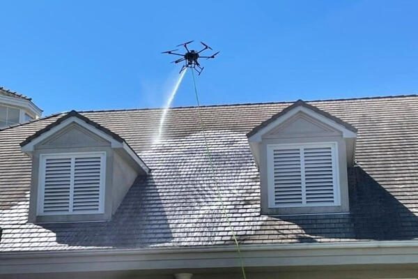 Drone spraying water on a rooftop under clear blue sky.