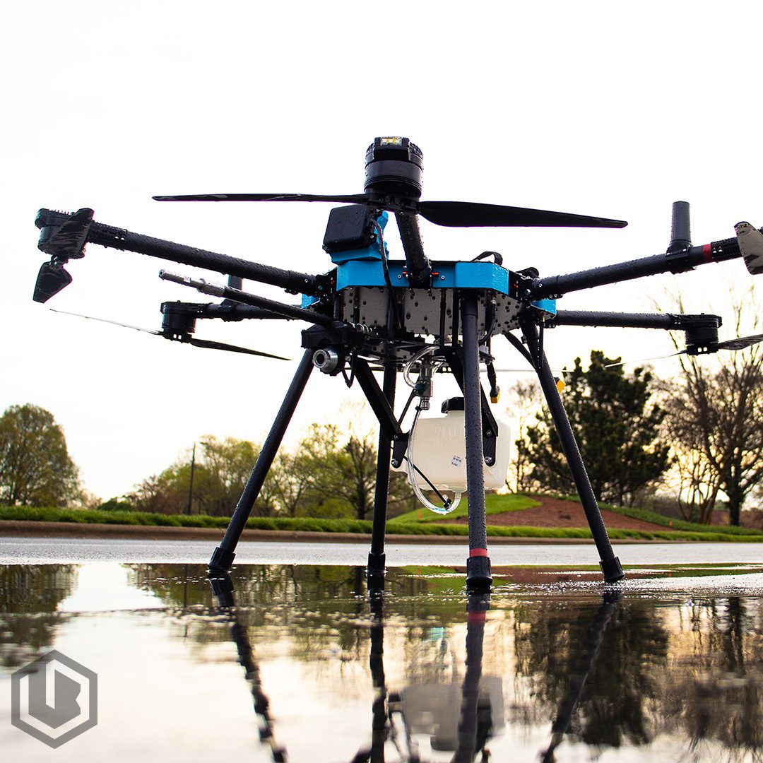 A professional drone with multiple rotors hovering over water near trees.