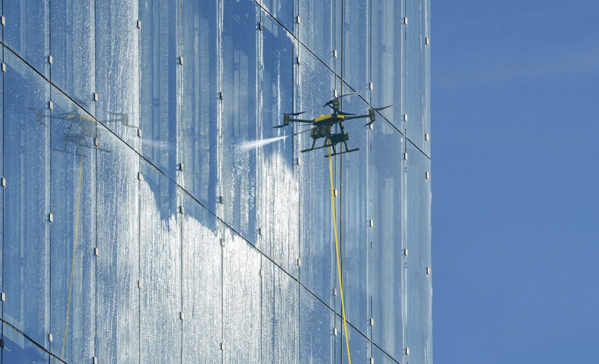Drone inspecting a large reflective glass building exterior with cables.