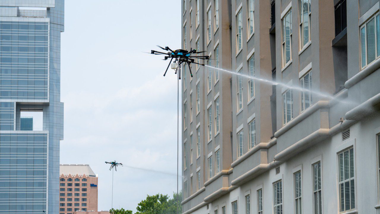 Drones cleaning building exterior with water jets.